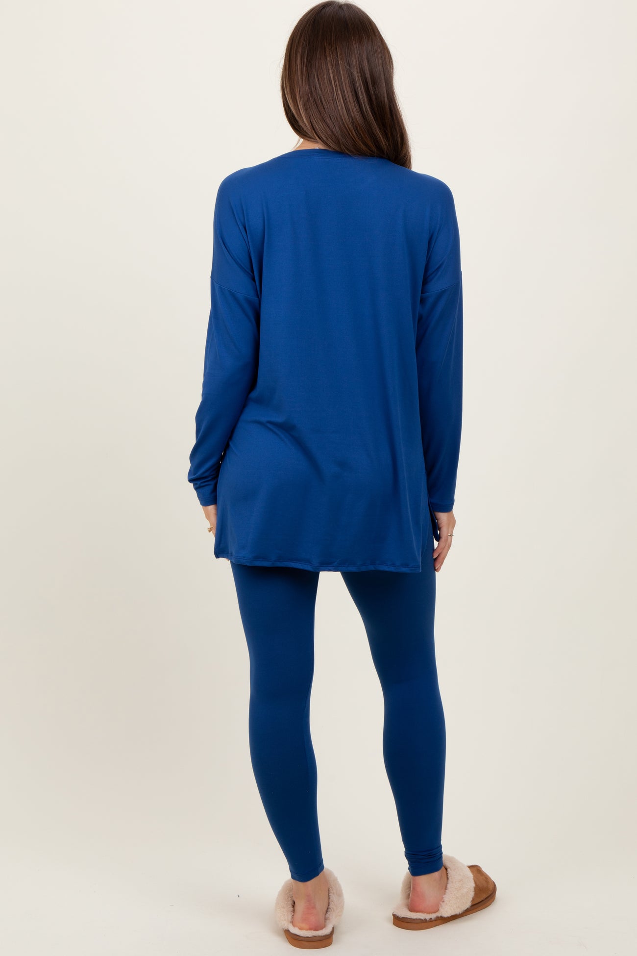 woman wearing a long sleeve blue maternity tunic top and matching blue leggings, standing with her back to the camera
