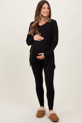 woman wearing a black maternity tunic top and black leggings, holding her baby bump, styled with cozy slippers