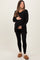 woman wearing a black maternity tunic top and black leggings, holding her baby bump, styled with cozy slippers