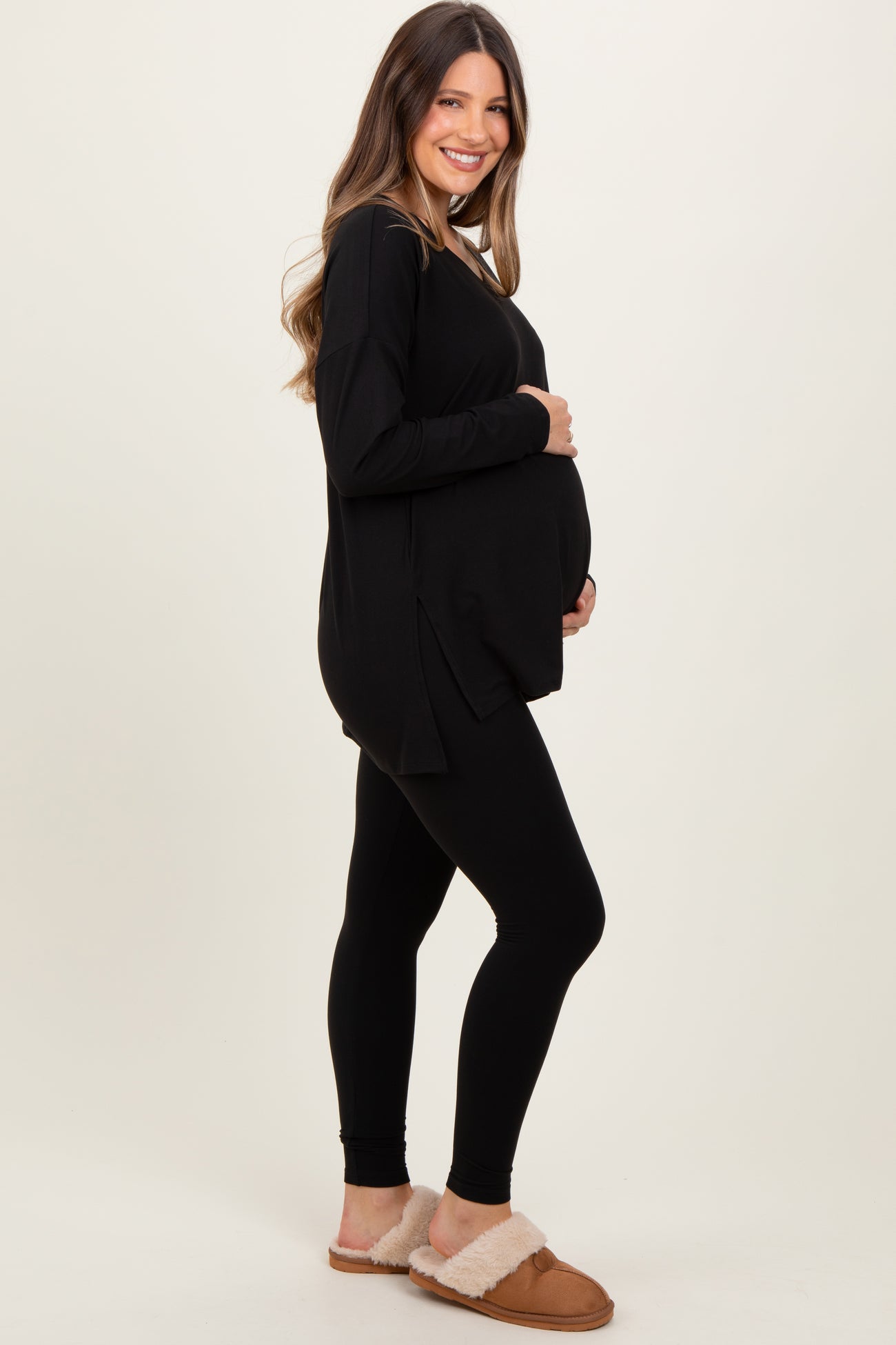 woman wearing a black long sleeve maternity top and black leggings, showing her baby bump, paired with cozy slippers