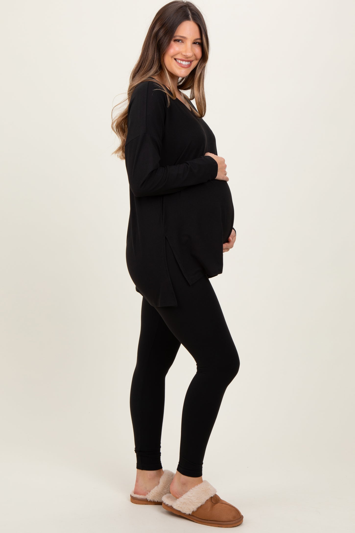 woman wearing a black long sleeve maternity top and black leggings, showing her baby bump, paired with cozy slippers