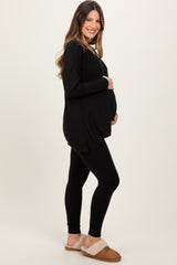woman wearing a black long sleeve maternity top and black leggings, showing her baby bump, paired with cozy slippers