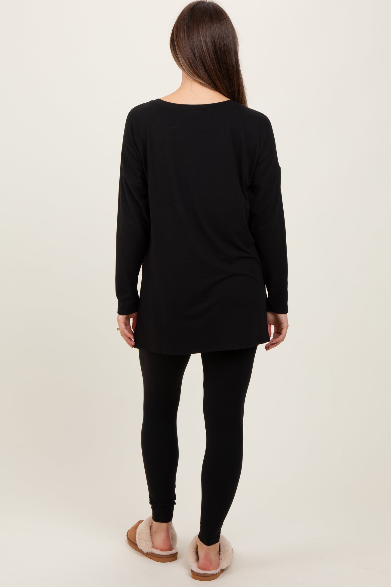 woman wearing a black long sleeve maternity tunic with black leggings and slippers, viewed from the back