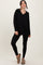 woman wearing a black long sleeve v-neck top and black leggings, with brown slip-on shoes