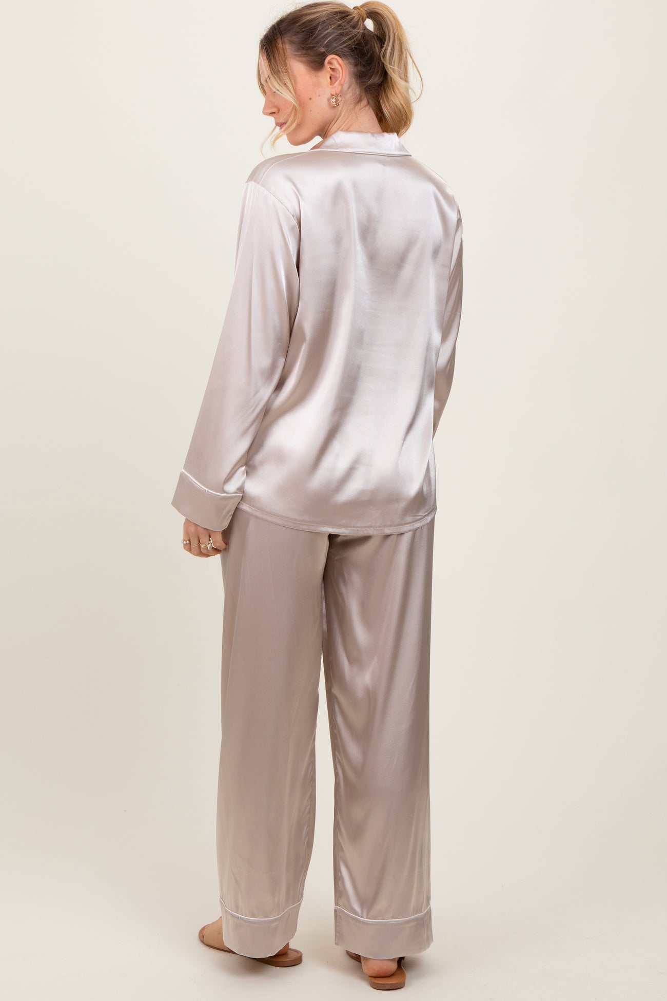 woman wearing a light beige satin pajama set with long sleeves and wide-leg pants, viewed from the back