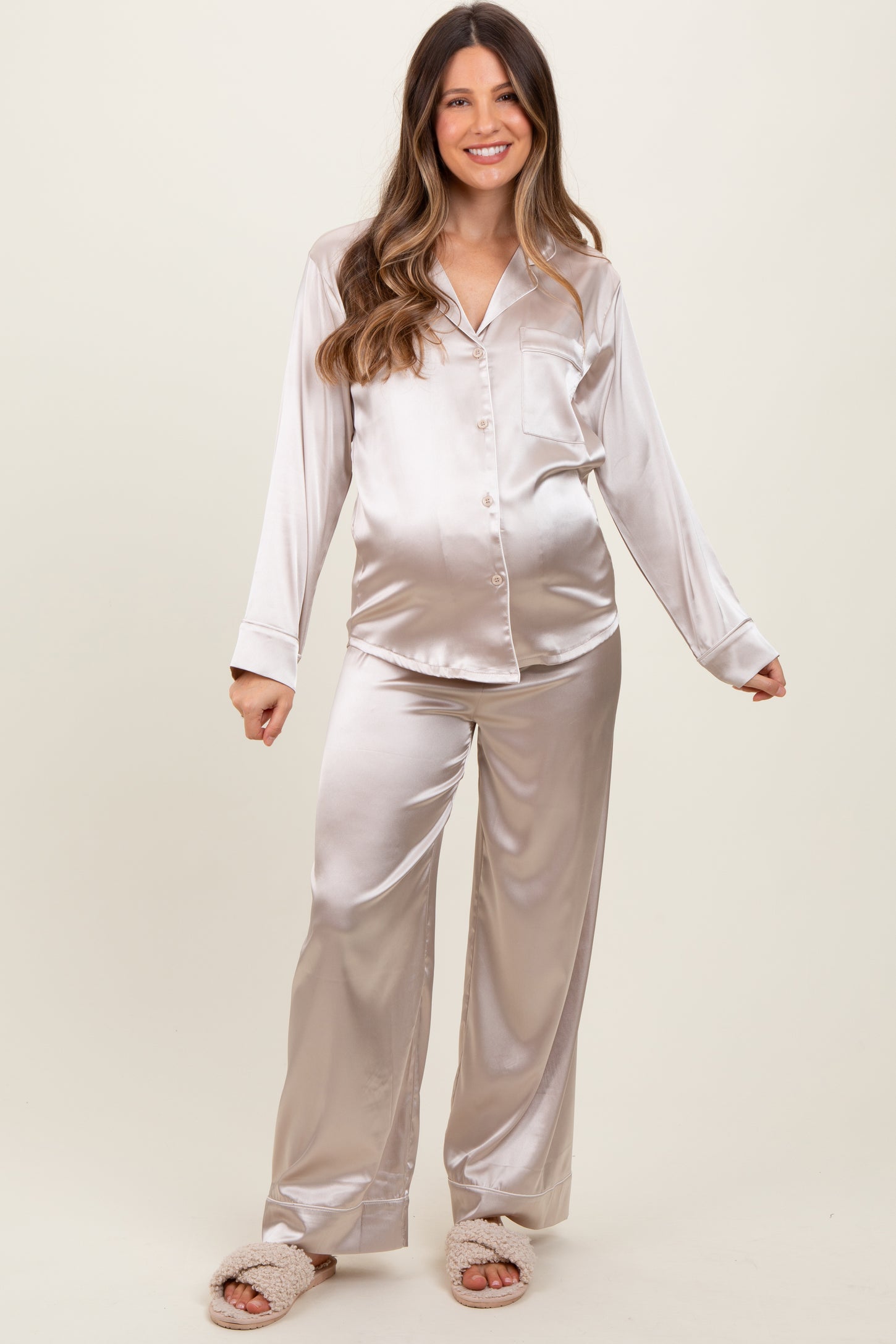 woman wearing a light beige satin maternity pajama set with long sleeves and pants, showcasing her baby bump