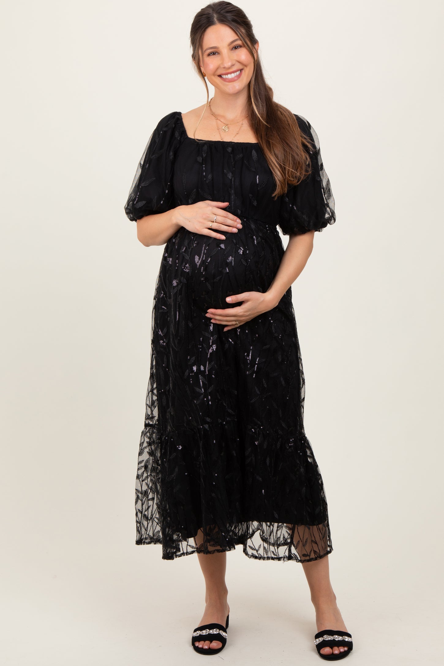 woman wearing a black puff sleeve maternity dress with a square neckline and holding her baby bump