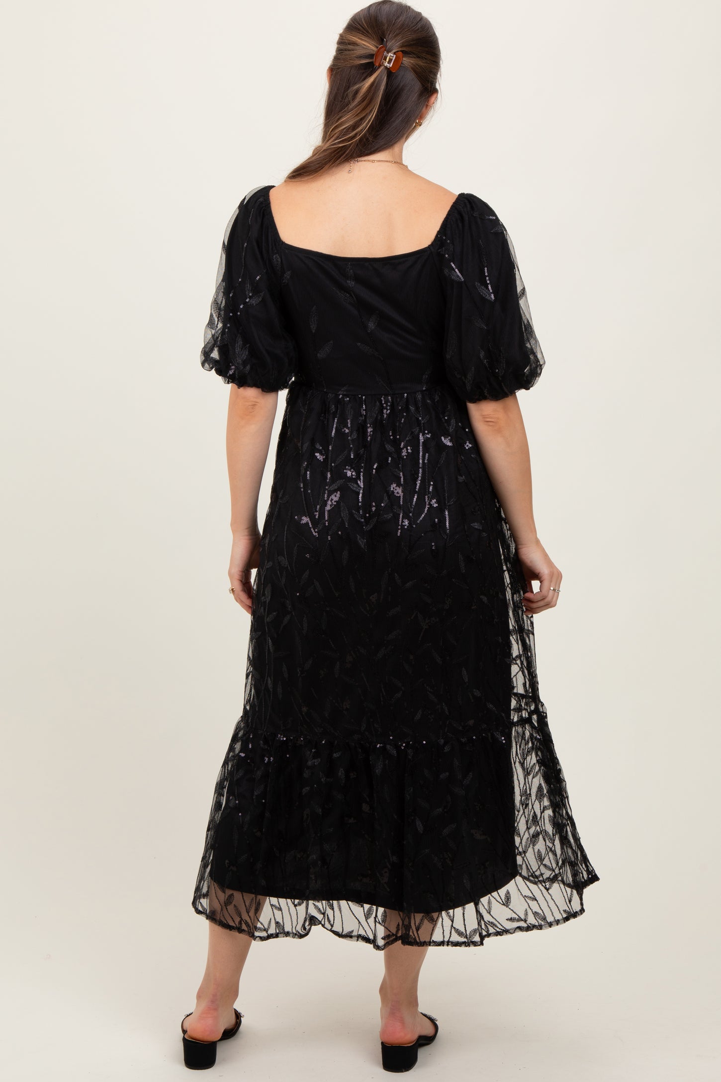 woman wearing a black maternity maxi dress with sheer puff sleeves and a ruffled hem, showing a baby bump from behind
