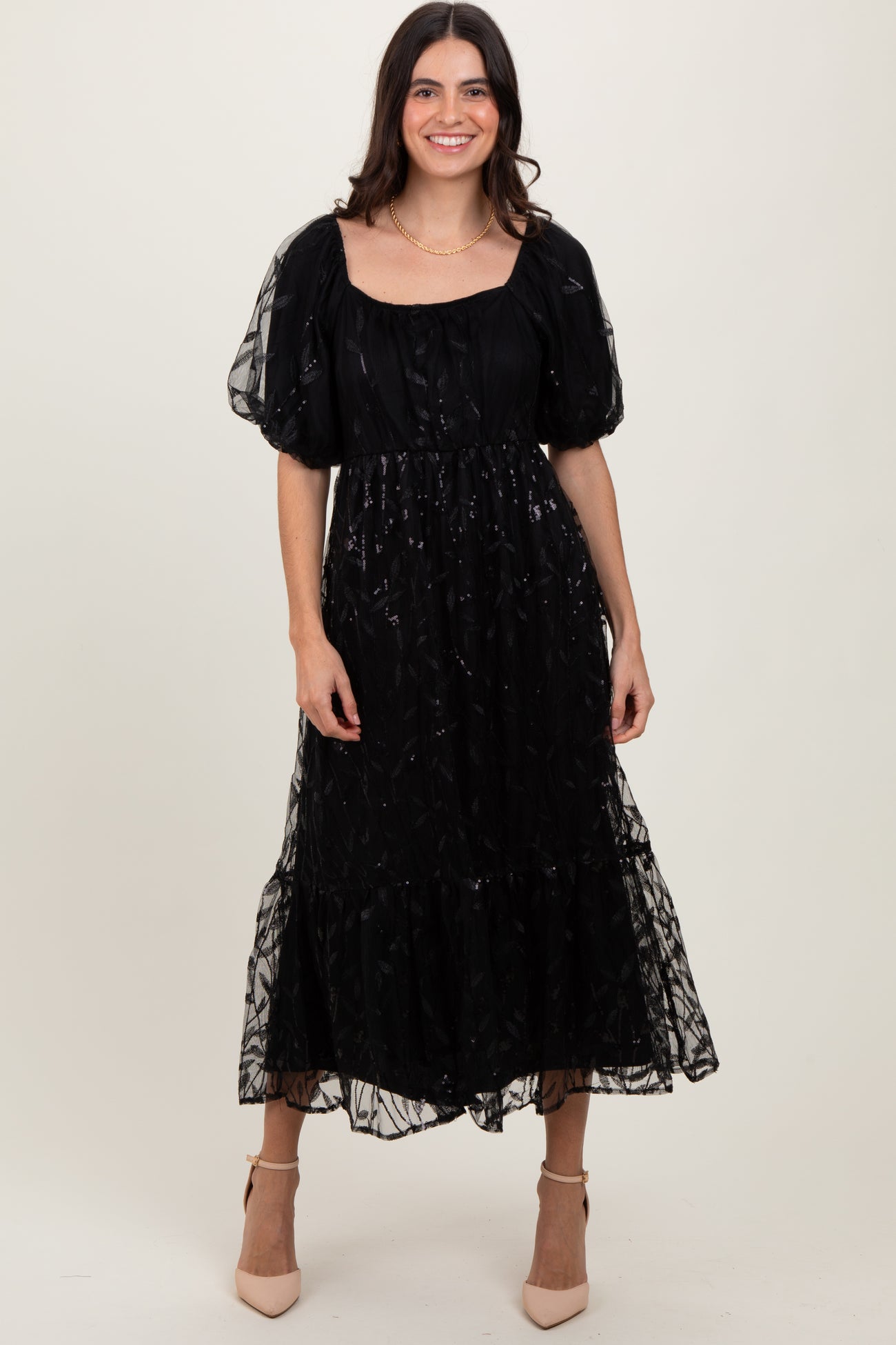woman wearing a black puff sleeve midi dress with sheer overlay and ruffled hem, standing and smiling