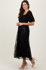 woman wearing a black puff sleeve maxi dress with floral embroidery and tiered skirt, paired with nude high heels