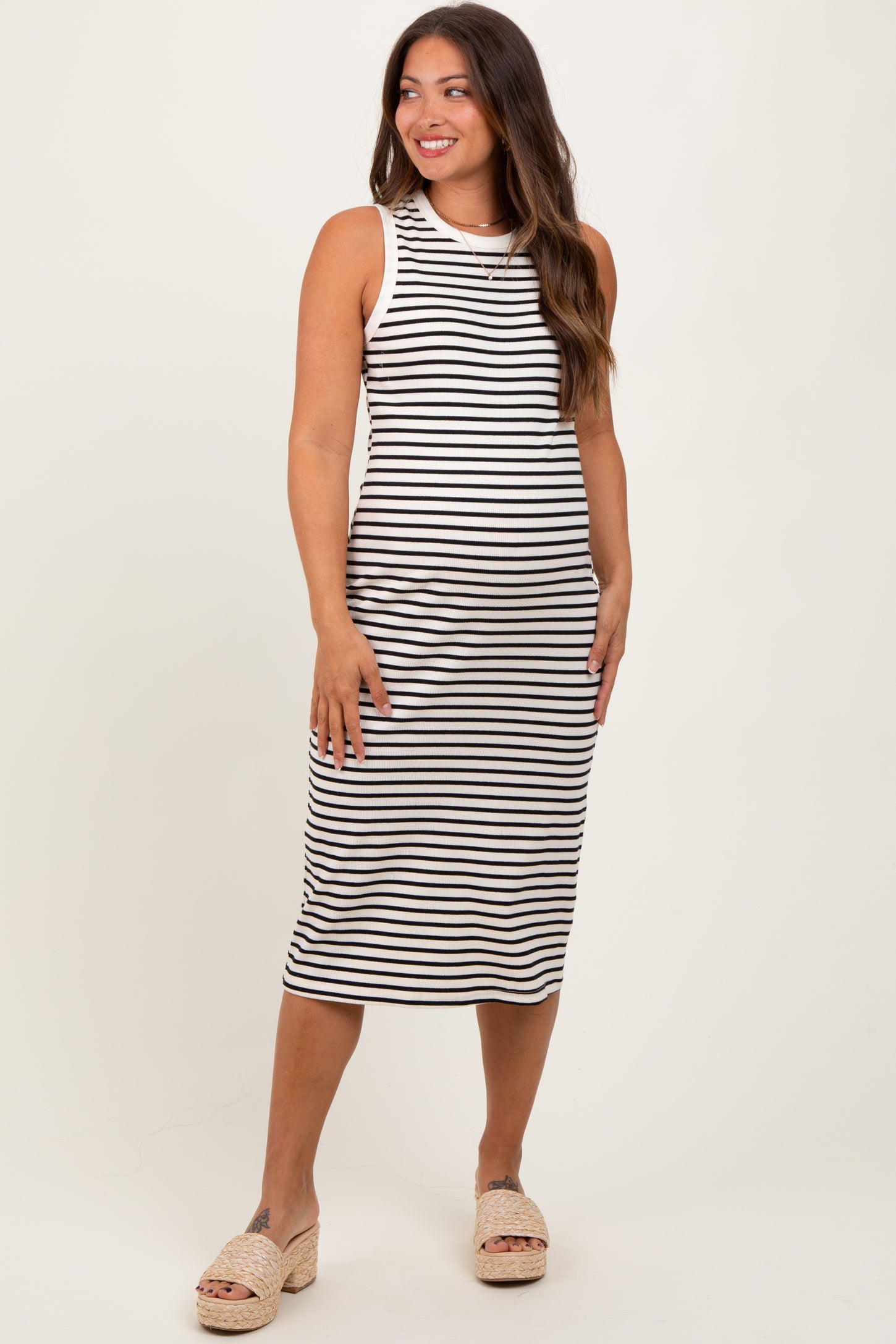 woman wearing a black and white striped maternity tank dress, standing and smiling, with a fitted silhouette