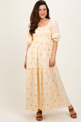 woman wearing a yellow puff sleeve maxi dress with floral details and a tiered skirt, standing against a neutral background