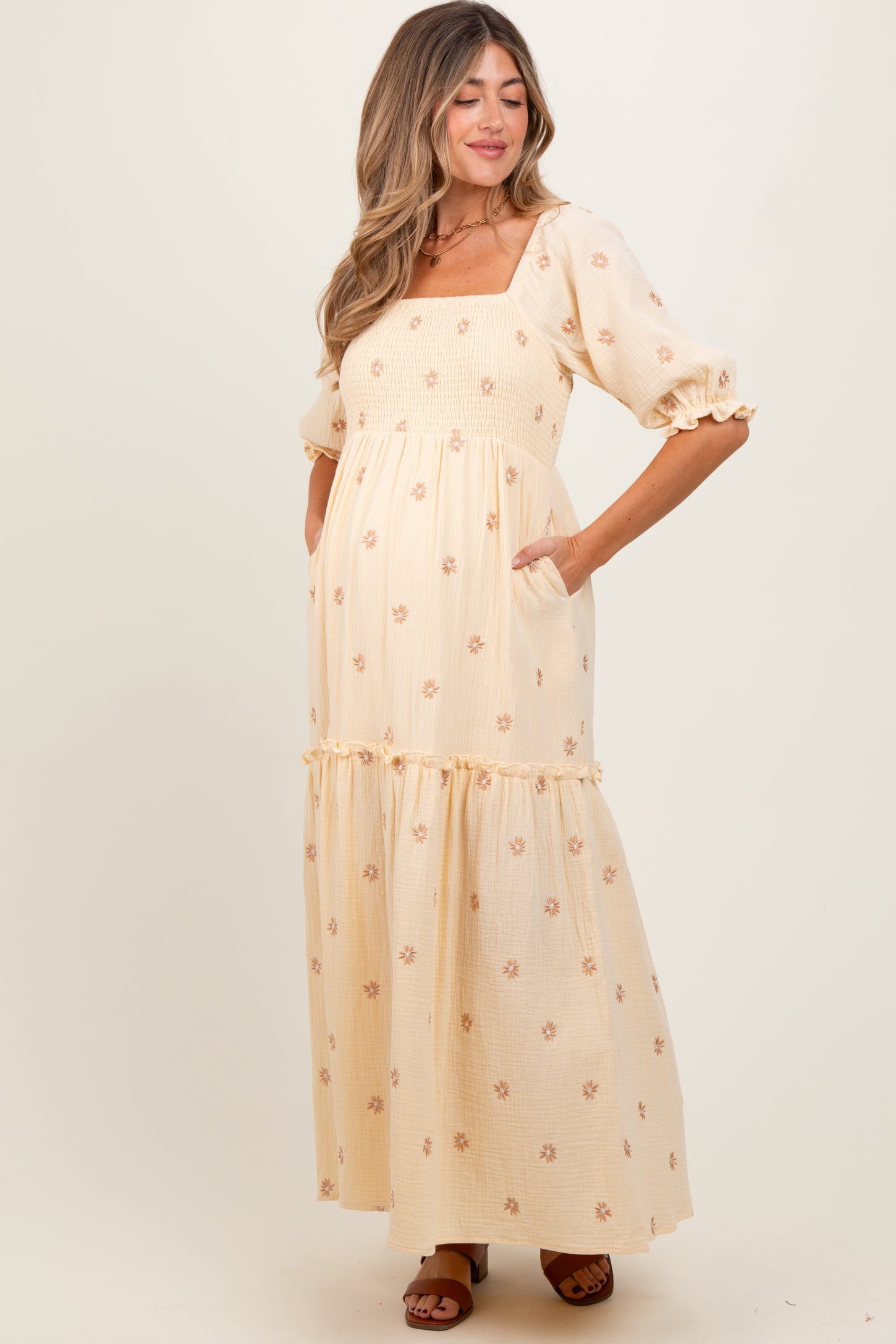 woman wearing a floral printed yellow maternity maxi dress with puff sleeves and pockets, showcasing her baby bump