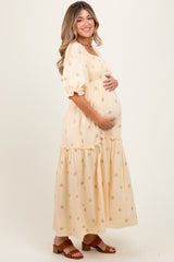 woman wearing a cream floral maternity dress with puff sleeves and a tiered skirt, cradling her baby bump