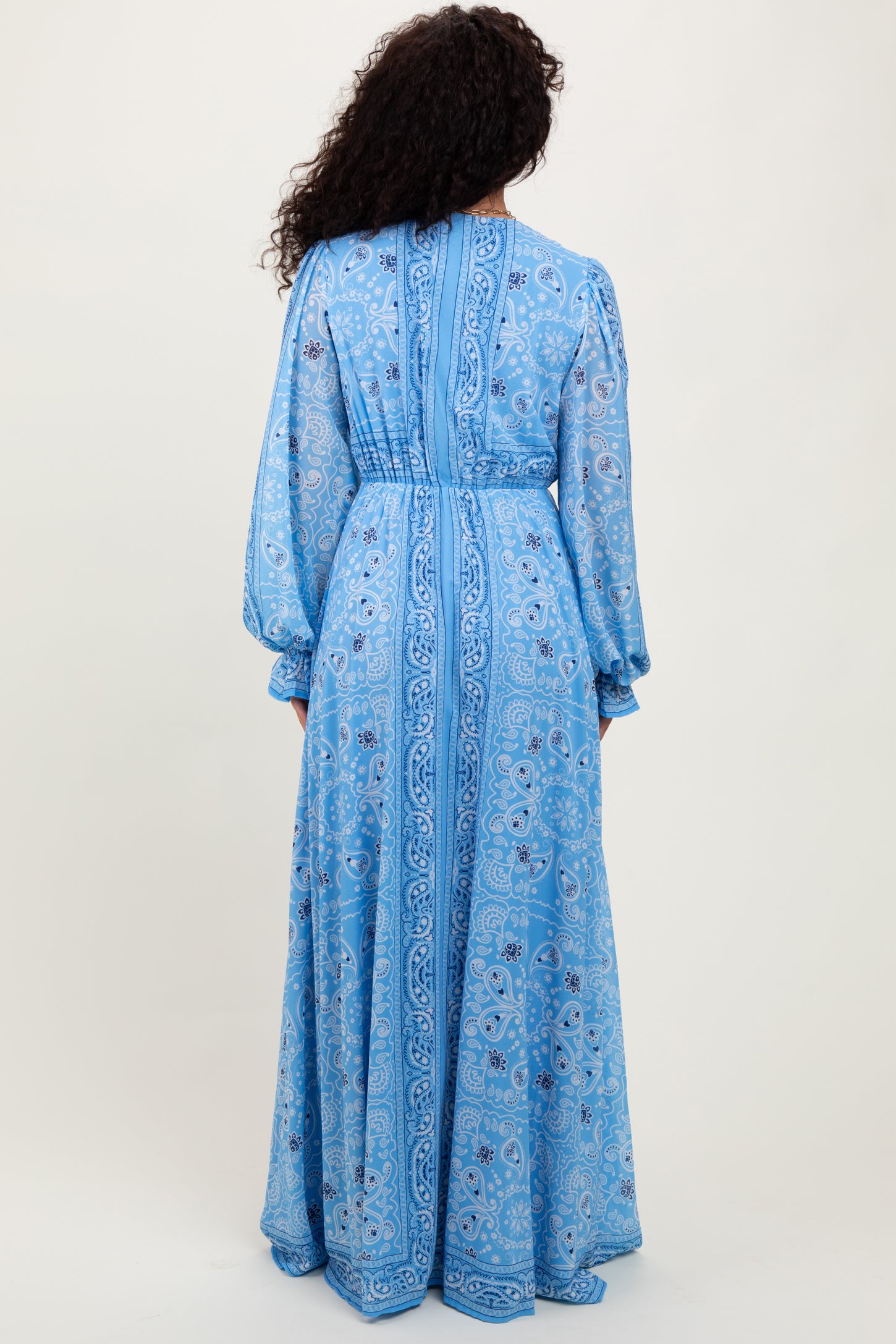 woman wearing a long sleeve blue maxi dress with intricate white patterns and a fitted waist design