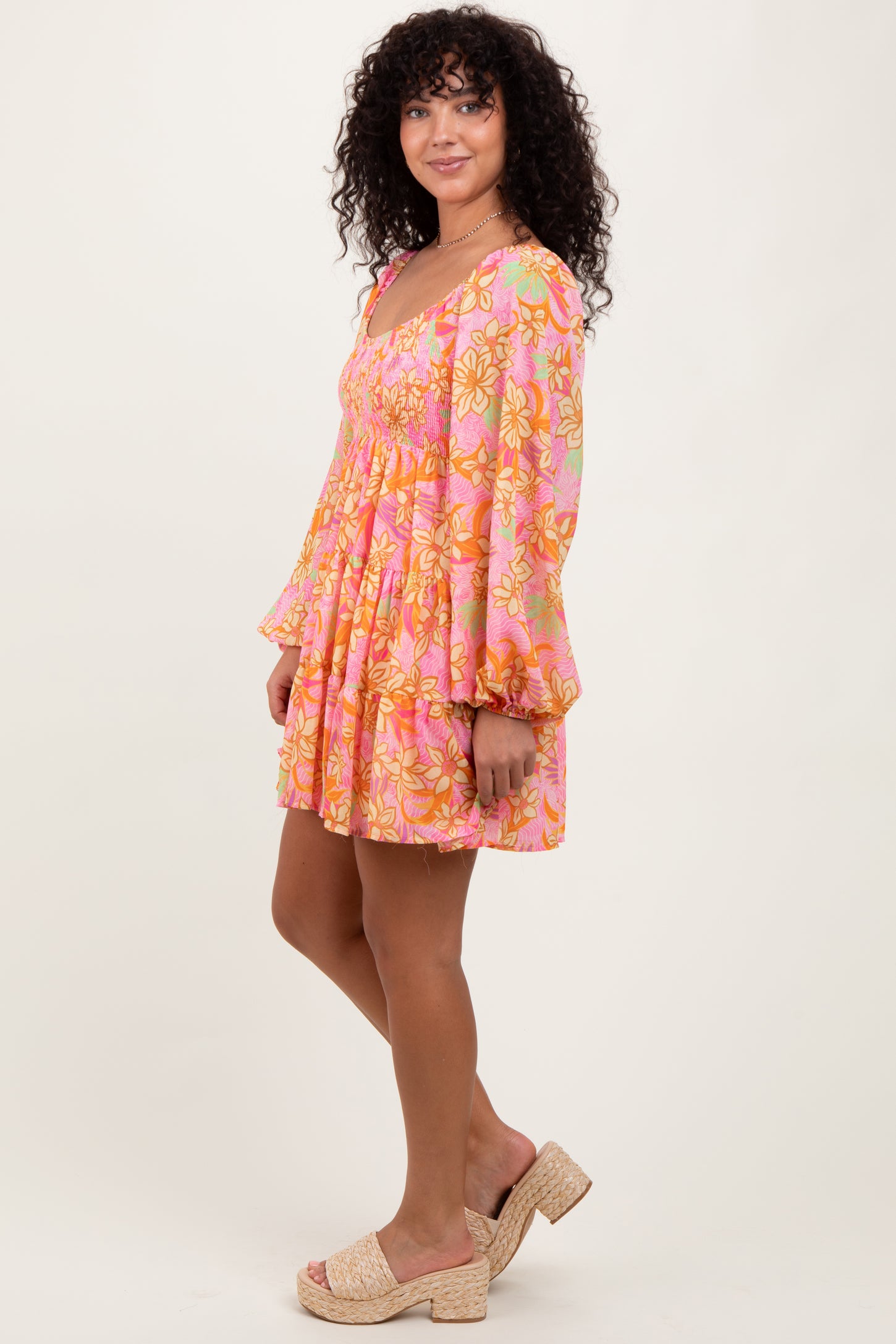 woman wearing a pink floral mini dress with flared sleeves and a cinched waist, standing sideways