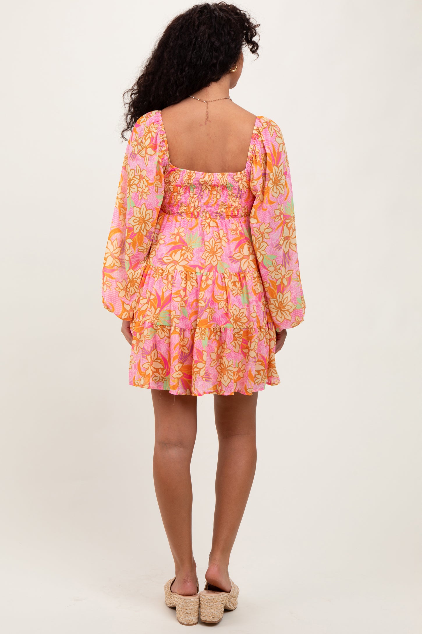 woman wearing a pink floral mini dress with long sleeves and a tiered skirt, seen from the back