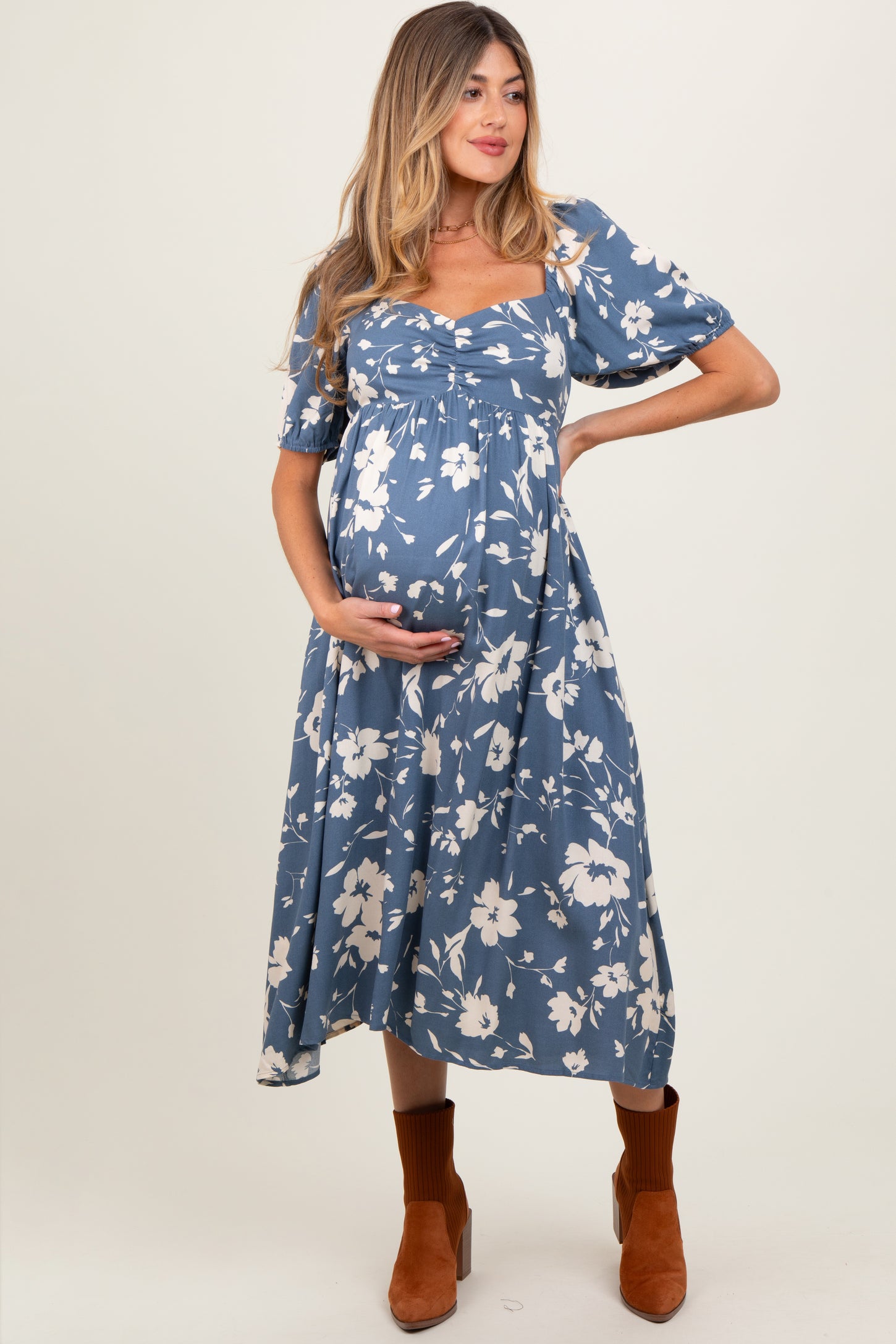 woman wearing a blue floral print maternity dress with puff sleeves and a baby bump, styled with brown ankle boots