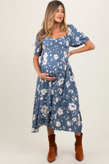 woman wearing a blue floral print maternity dress with puff sleeves and a baby bump, styled with brown ankle boots