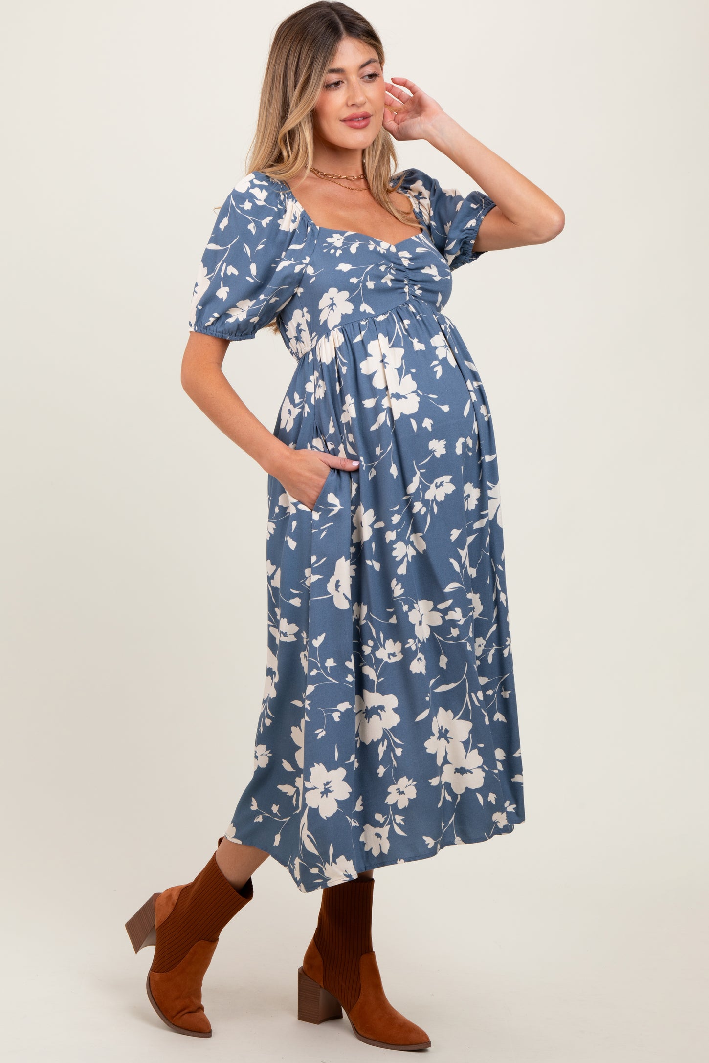 woman wearing a blue floral maternity dress with puff sleeves and pockets, highlighting her baby bump