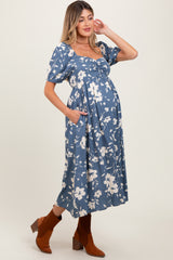 woman wearing a blue floral maternity dress with puff sleeves and pockets, highlighting her baby bump