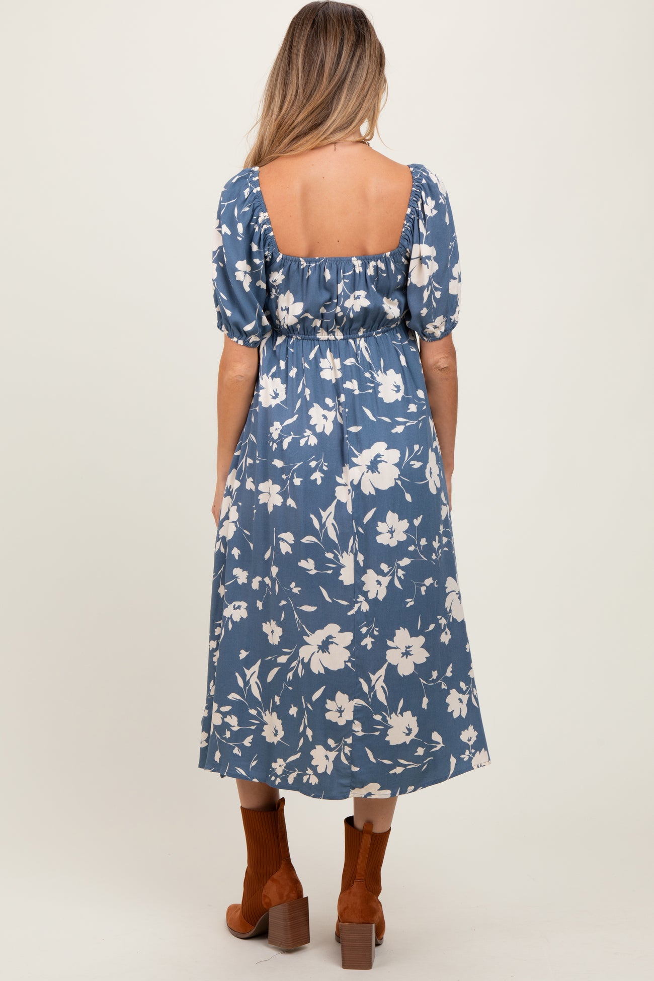 woman wearing a blue floral maternity dress with puff sleeves and a back cutout, styled with brown ankle boots