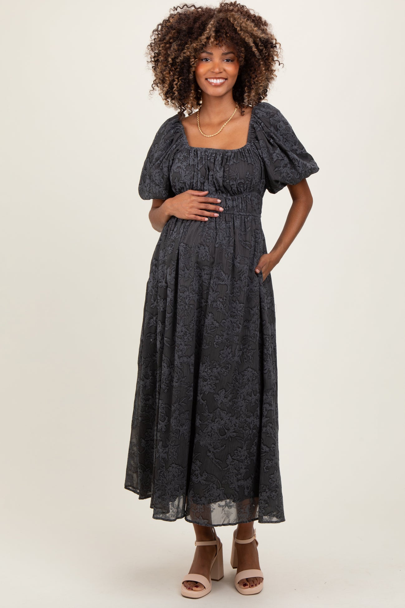 woman wearing a black floral maternity maxi dress with puff sleeves and a gathered waist, holding her baby bump