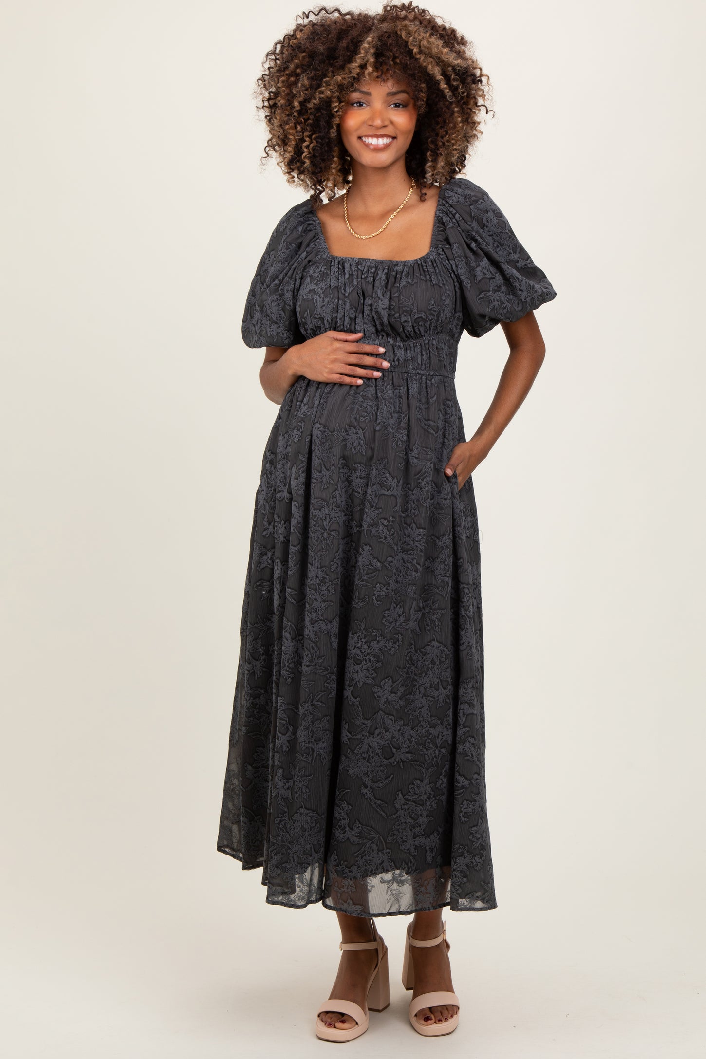 woman wearing a black floral maternity maxi dress with puff sleeves and a gathered waist, holding her baby bump