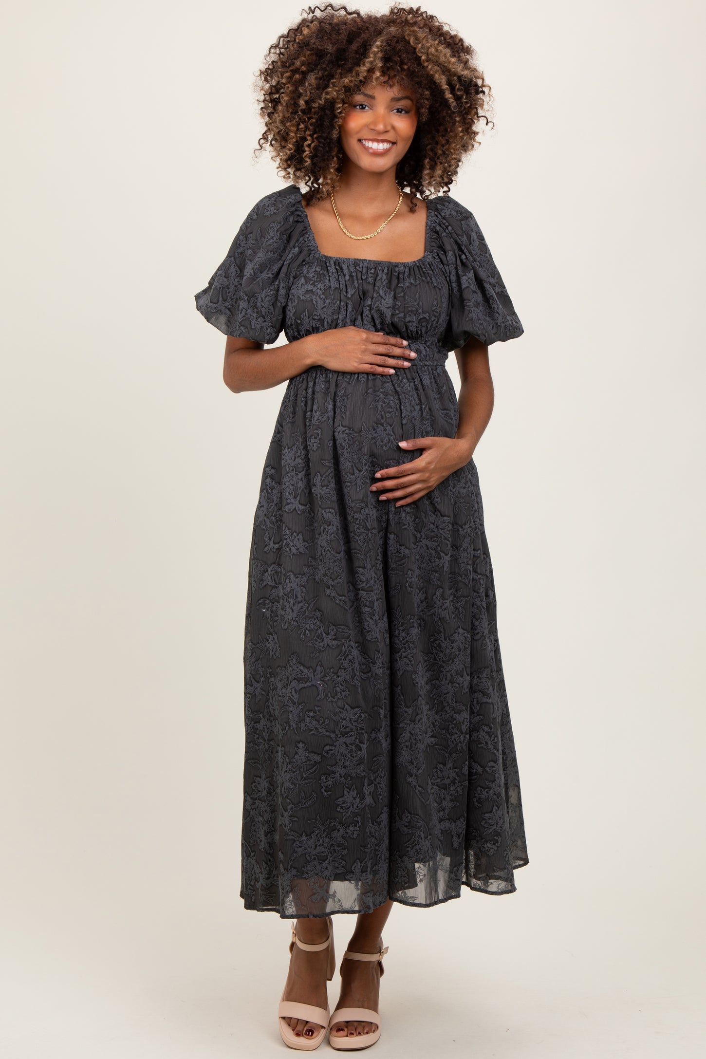 woman wearing a dark gray floral maternity dress with puff sleeves and holding her baby bump