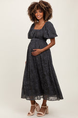 woman wearing a dark gray floral maternity dress with puff sleeves and holding her baby bump