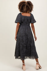 woman wearing a dark gray floral maternity dress with puff sleeves and a smocked waist, showing a baby bump
