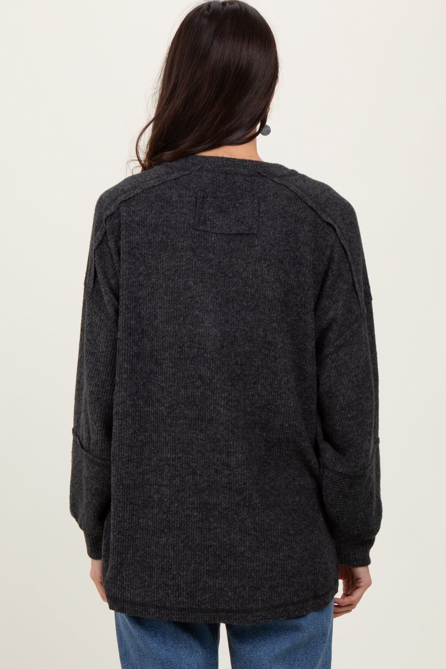 woman wearing a dark gray oversized sweater with long sleeves and a relaxed fit, viewed from the back