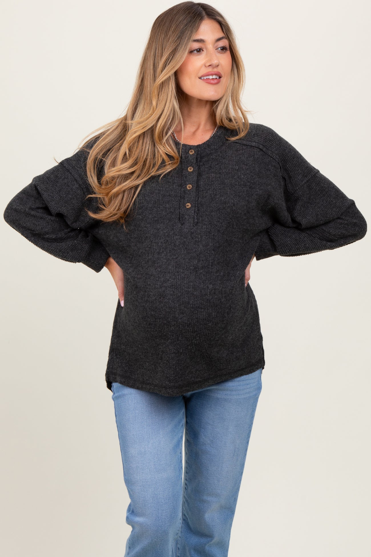 woman wearing a dark gray maternity henley top with buttons and a visible baby bump, paired with light blue jeans