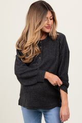 woman wearing a dark gray maternity long sleeve top with buttons, gently pulling up the sleeve to reveal her baby bump