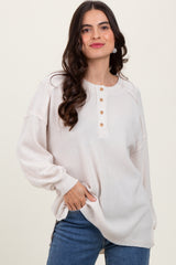 woman wearing a light beige oversized sweater with a henley neckline and button details, paired with blue jeans