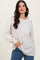 woman wearing a light beige oversized sweater with a henley neckline and button details, paired with blue jeans