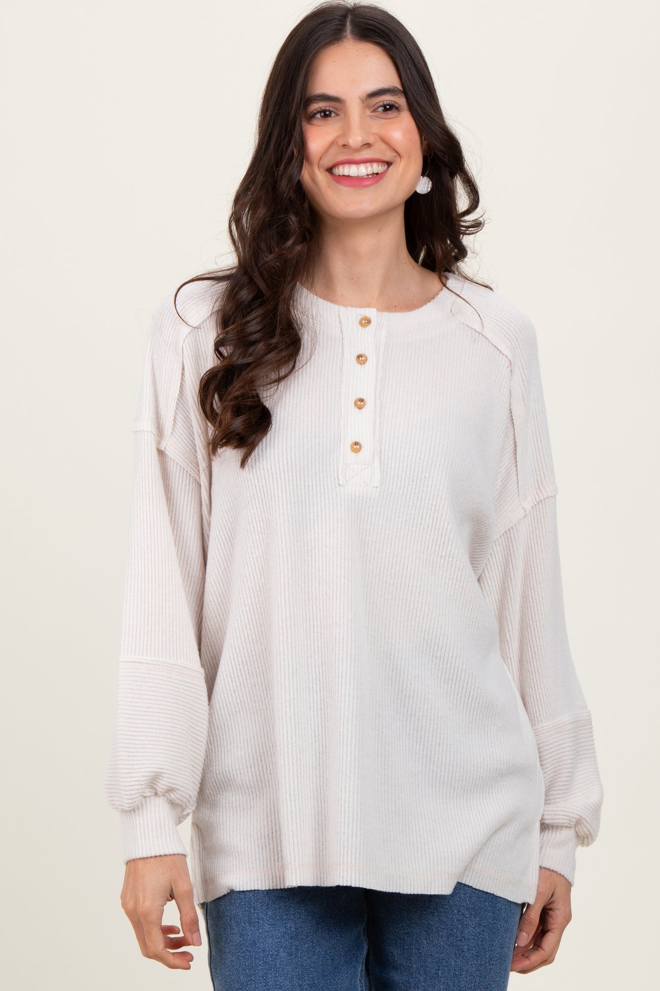 woman wearing a light beige long sleeve top with button detail and relaxed fit, smiling against a neutral background