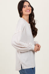 woman wearing a light beige ribbed long sleeve top with button detail and side slits, smiling at the camera