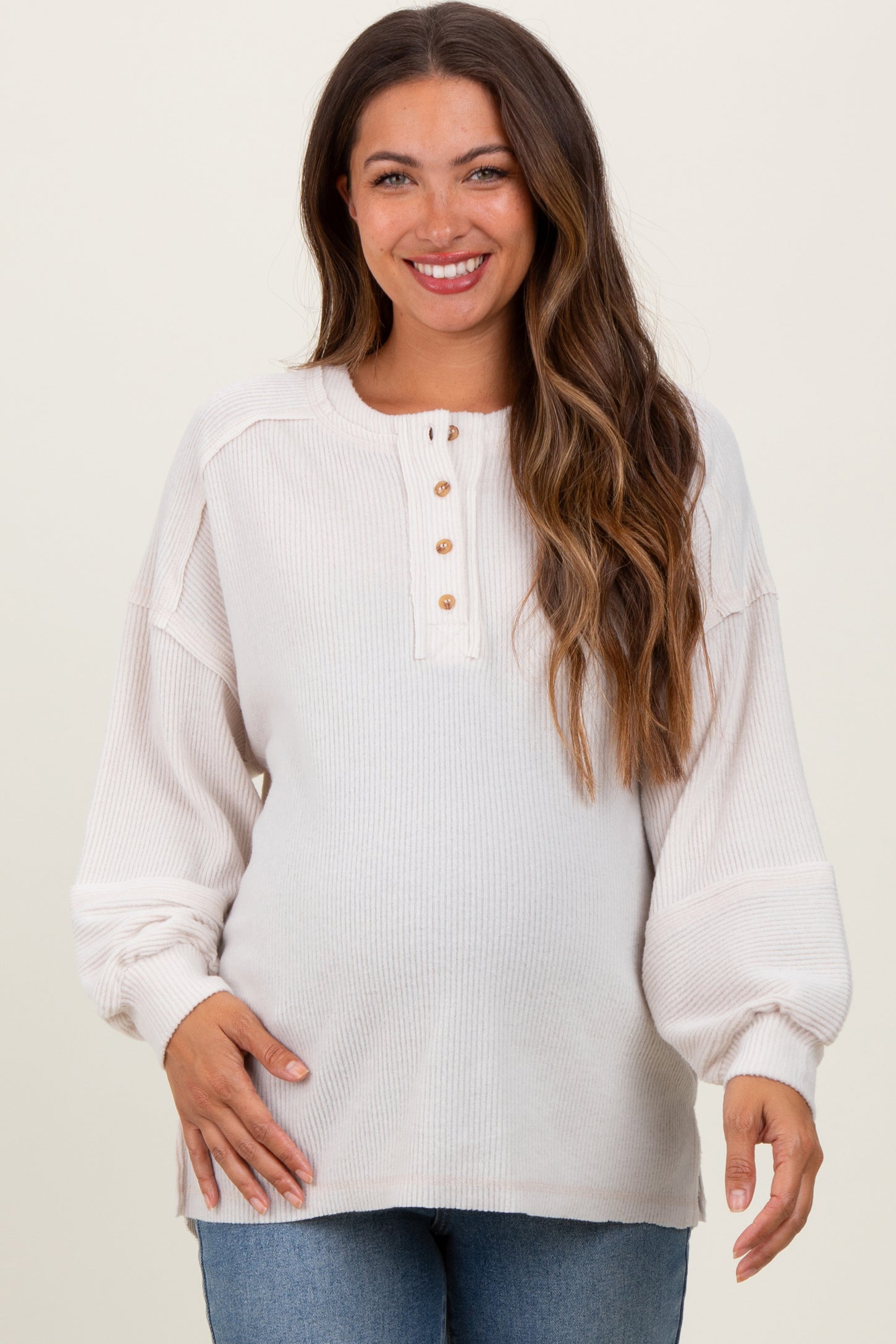 woman wearing a light beige maternity long sleeve top with buttons, showcasing her baby bump