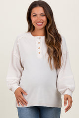 woman wearing a light beige maternity long sleeve top with buttons, showcasing her baby bump