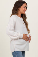 woman wearing a light beige long sleeve maternity top with buttons, holding her baby bump
