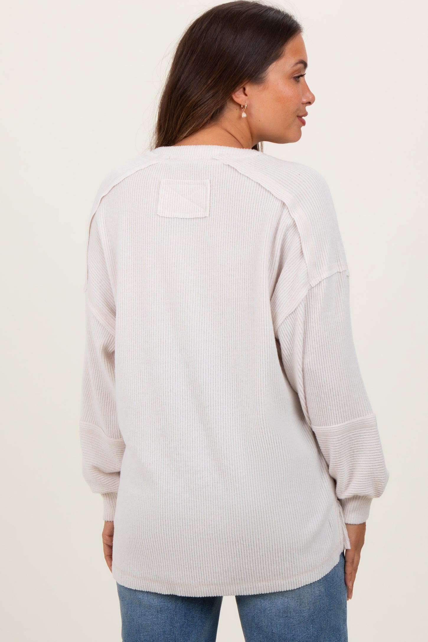 woman wearing a light beige maternity top with long sleeves and a relaxed fit, showing the back view