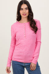 woman wearing a bright pink long sleeve ribbed top with a button detail neckline and styled hair