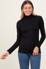 woman wearing a black long sleeve turtleneck top and blue jeans, smiling and posing with one hand out