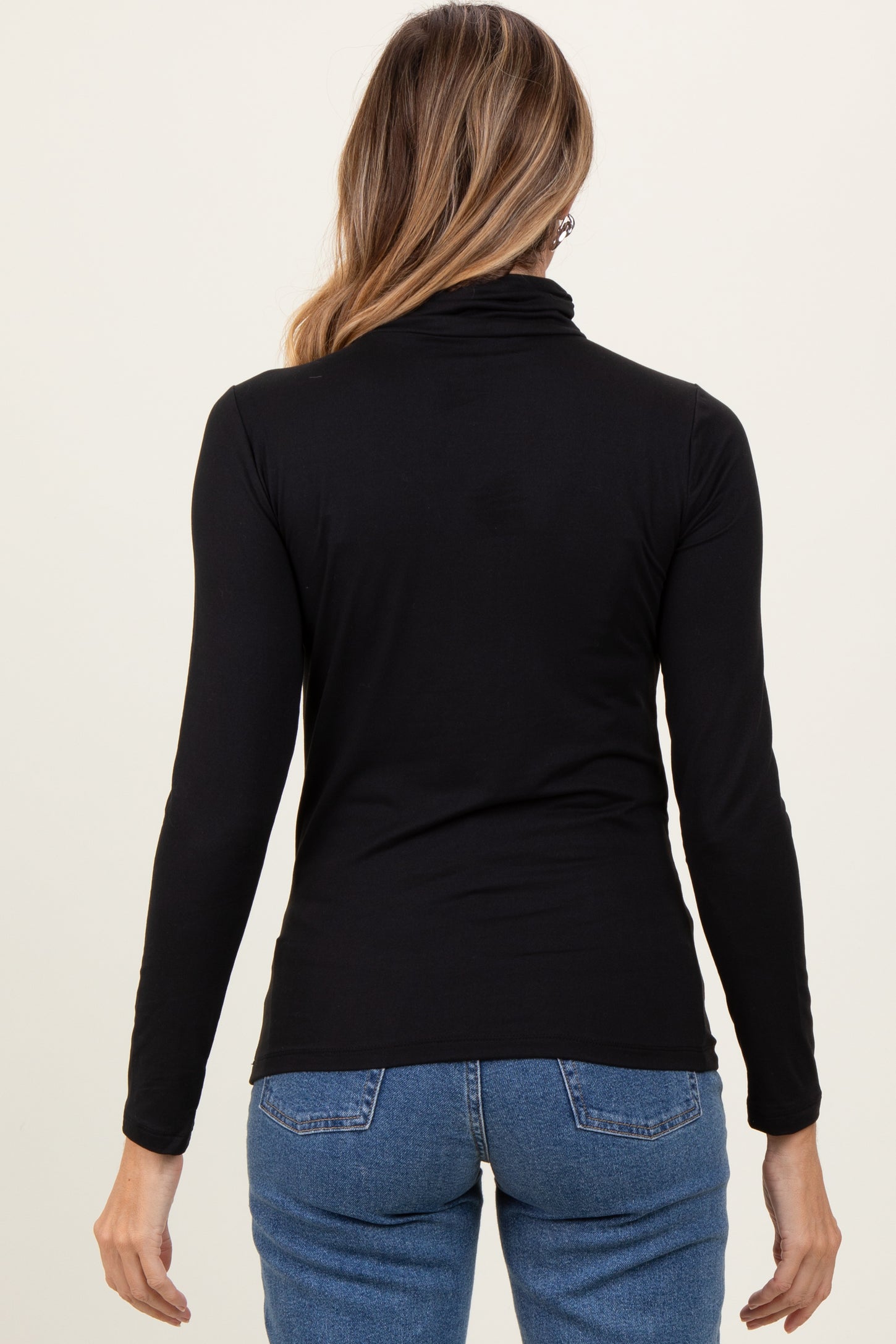 woman wearing a black long sleeve turtle neck top with a fitted style and back view, paired with blue jeans