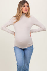 woman wearing a beige long sleeve maternity top and showing her baby bump with blue jeans