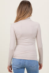 woman wearing a light beige maternity long sleeve top, viewed from the back, paired with blue jeans