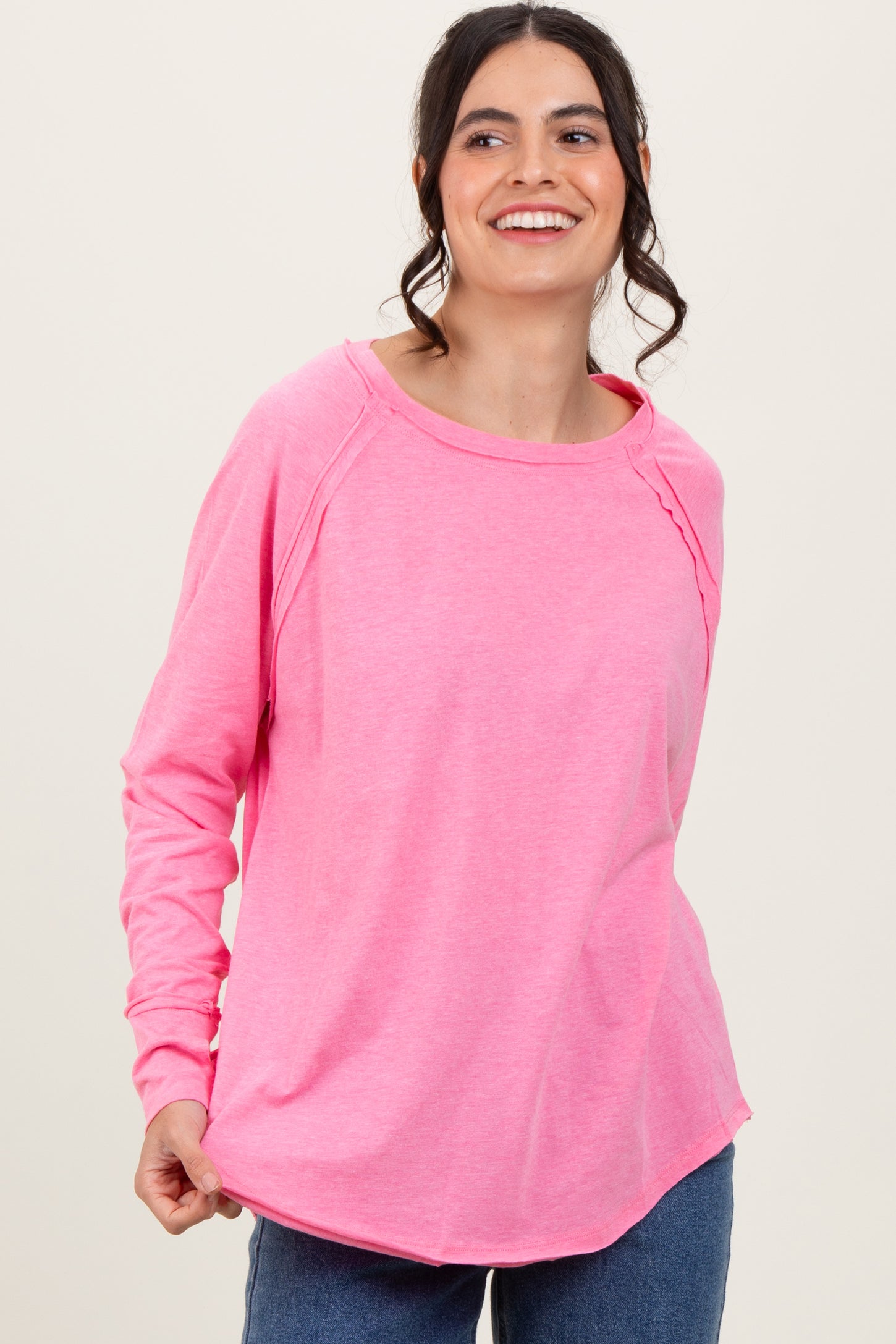 woman wearing a bright pink long sleeve top with a rounded neckline and relaxed fit, smiling at the camera