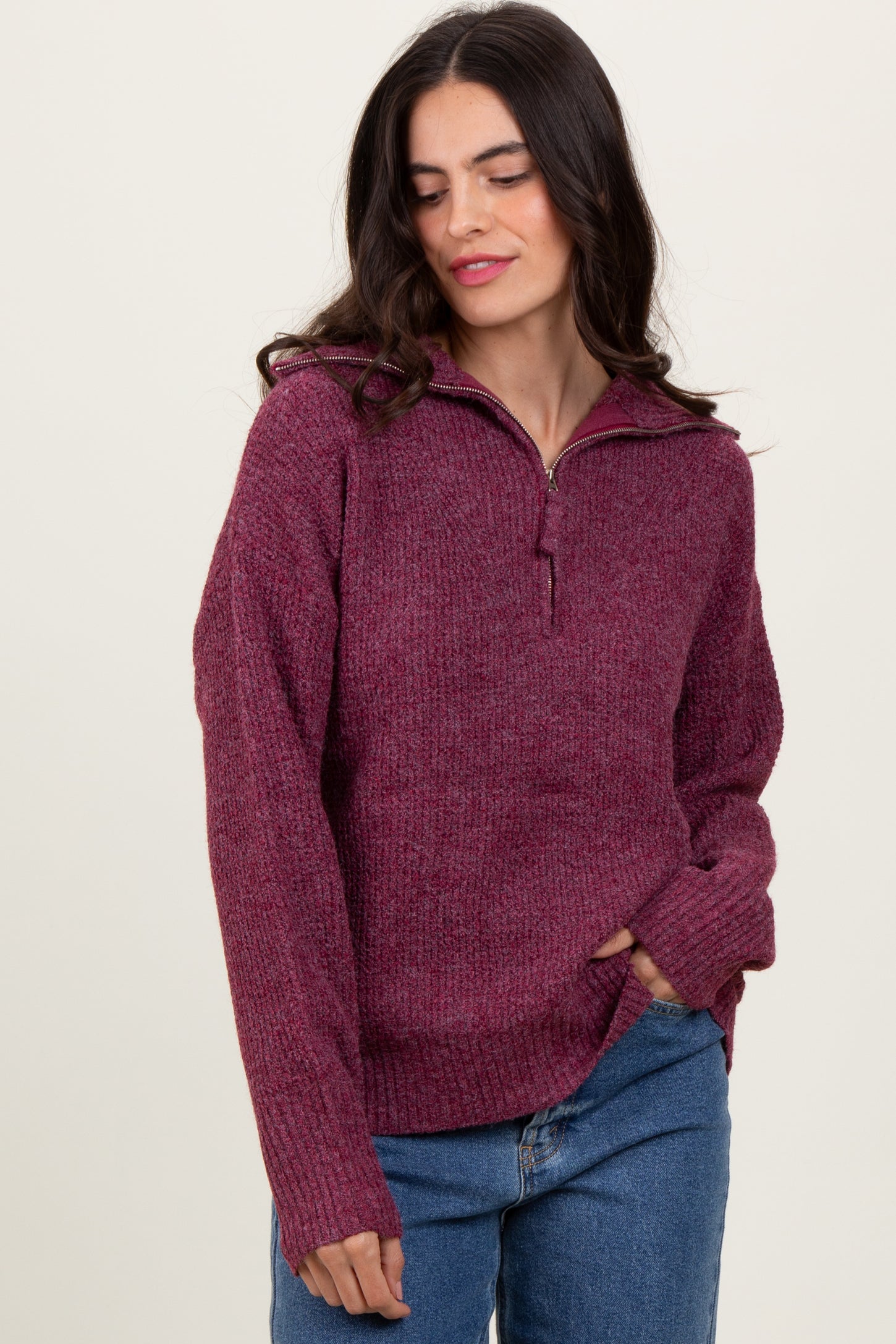 woman wearing a maroon zip-up sweater with a textured finish and relaxed fit, paired with blue jeans