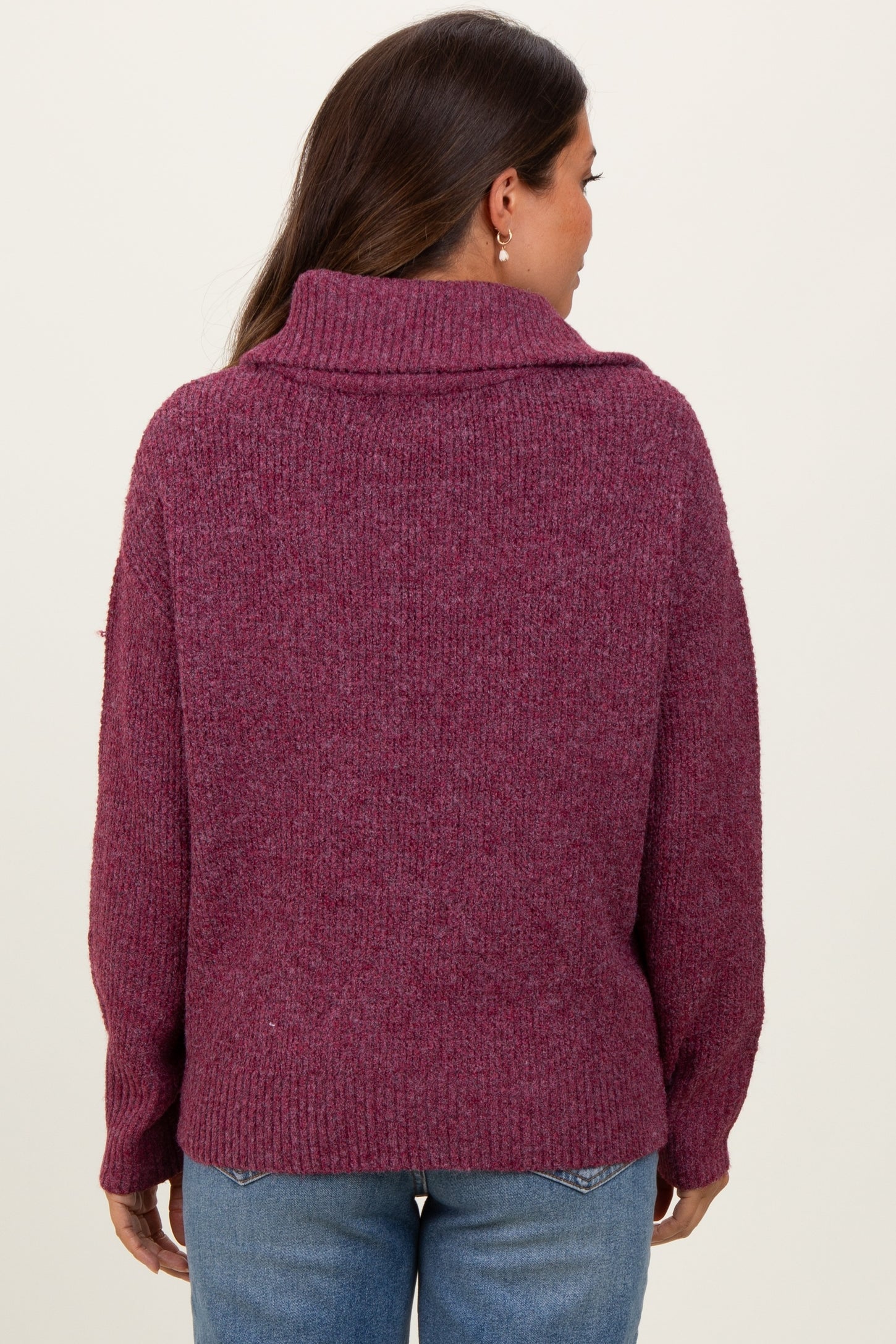 woman wearing a burgundy oversized maternity sweater with a high collar, viewed from the back